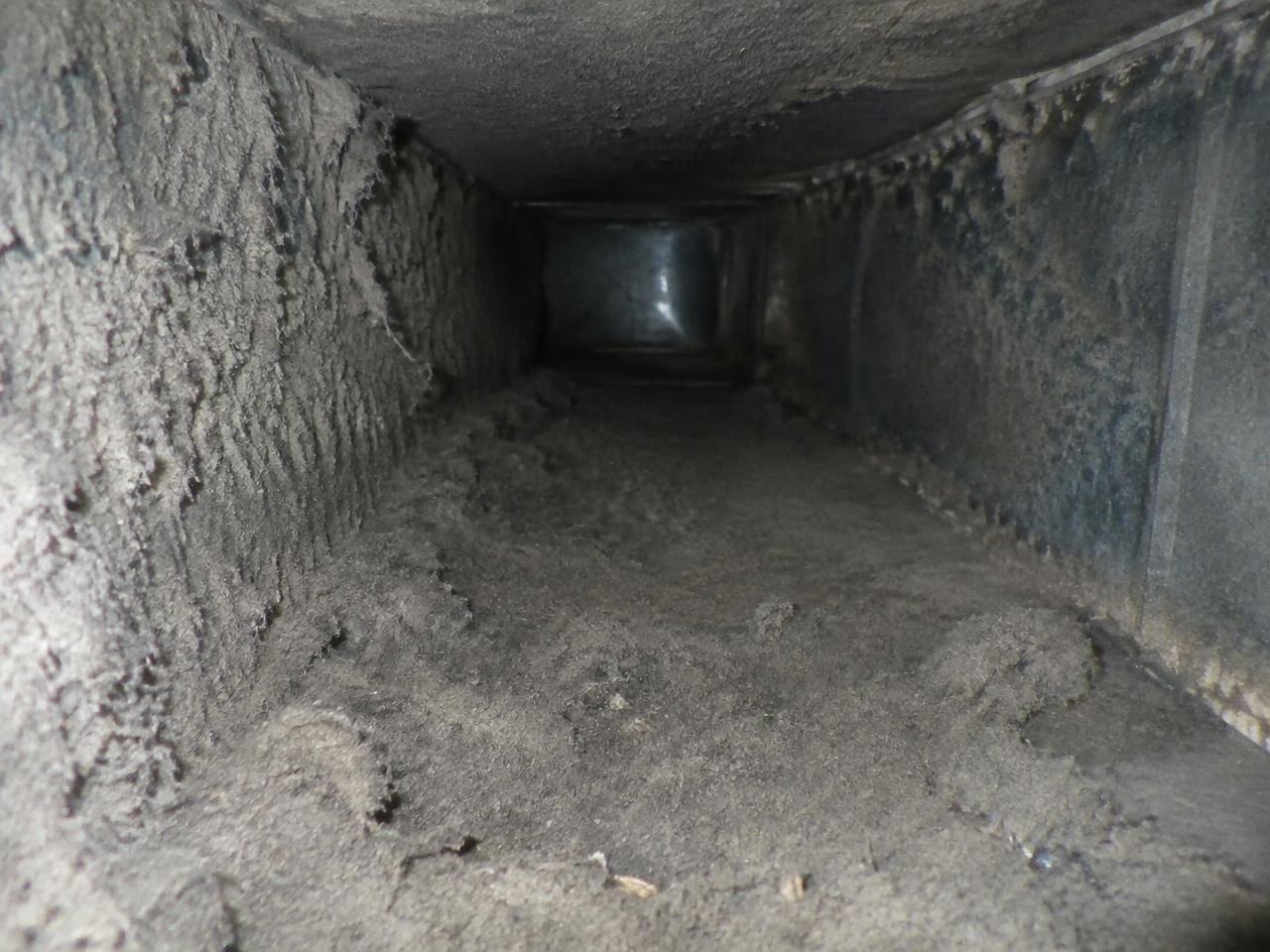 Interior de un ducto de aire antes de la limpieza, con la chapa metálica cubierta de polvo gris