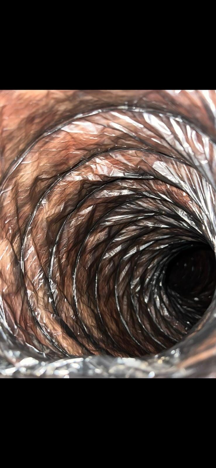 El interior de un ducto flexible, con la pared corrugada manchada de marrón, perdiéndose en la oscuridad