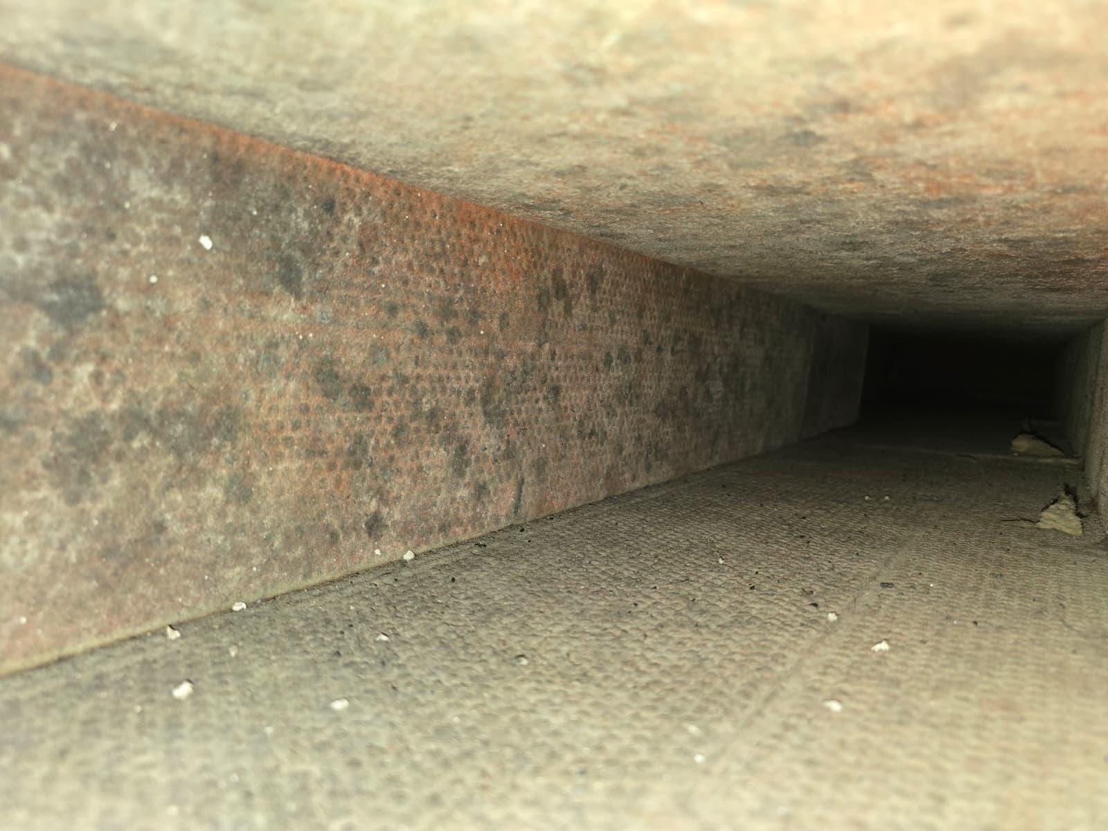 Looking down the inside of a rectangular duct run, its walls rust-stained, the passage receding into darkness